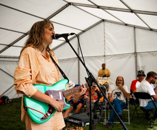 A singer playing a mint-green electric guitar on the marquee stage