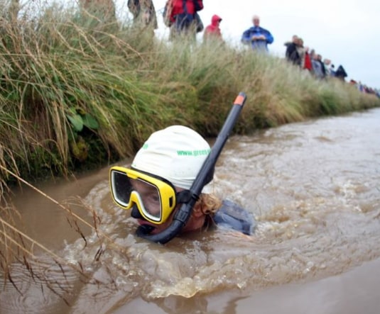 A competitor in a snorkel and mask swimming through the peat-brown bog trench
