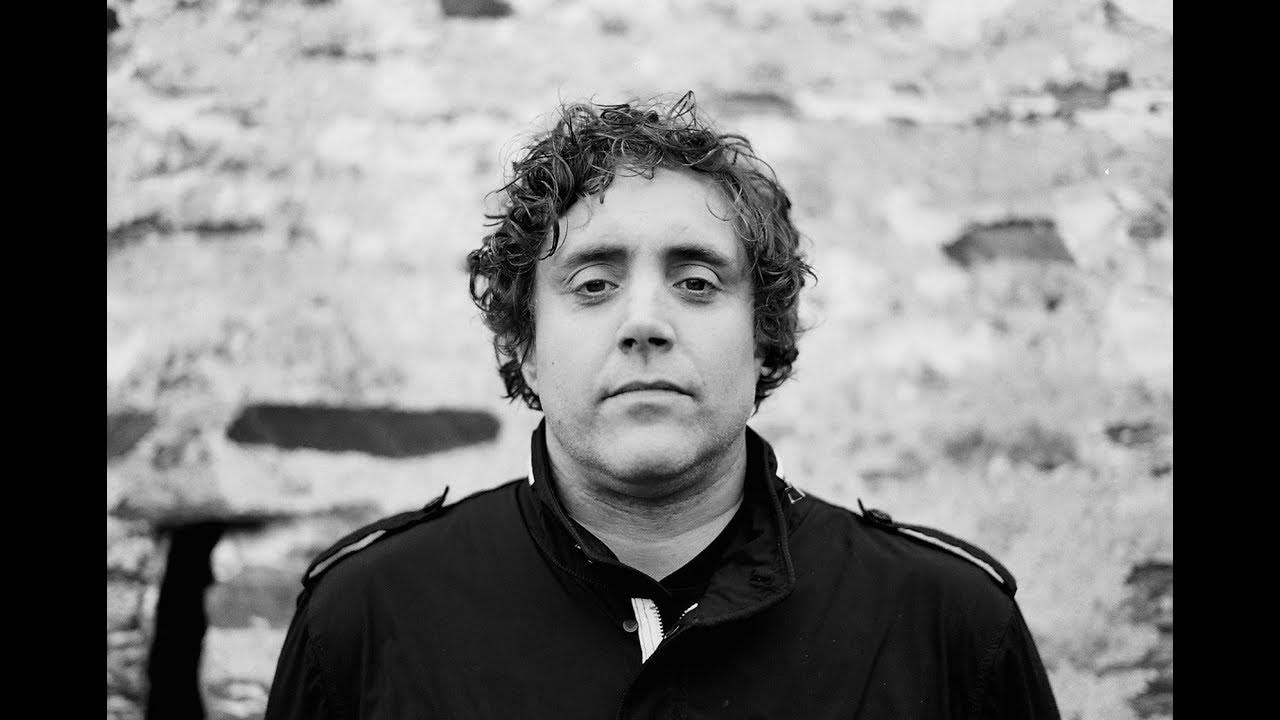 Black and white portrait of Ian, co-founder, against a stone wall