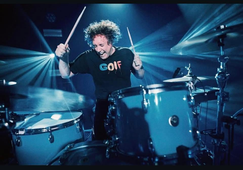 Ian performing live on drums with Kasabian under blue stage lights